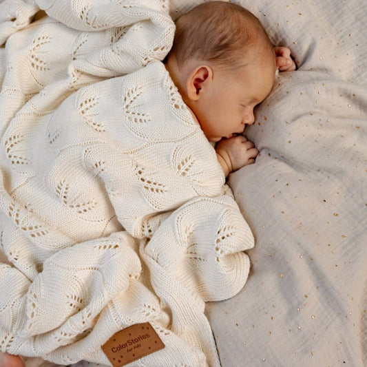 Baby der sover på maven pakket ind i et blødt, hvidt tæppe.