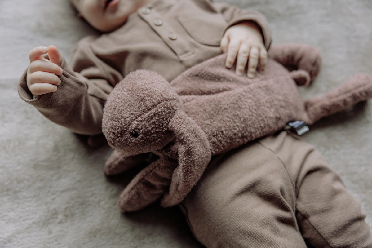 Barn med Flow Amsterdam Milo varmebamse i Chocolate liggende over maven.