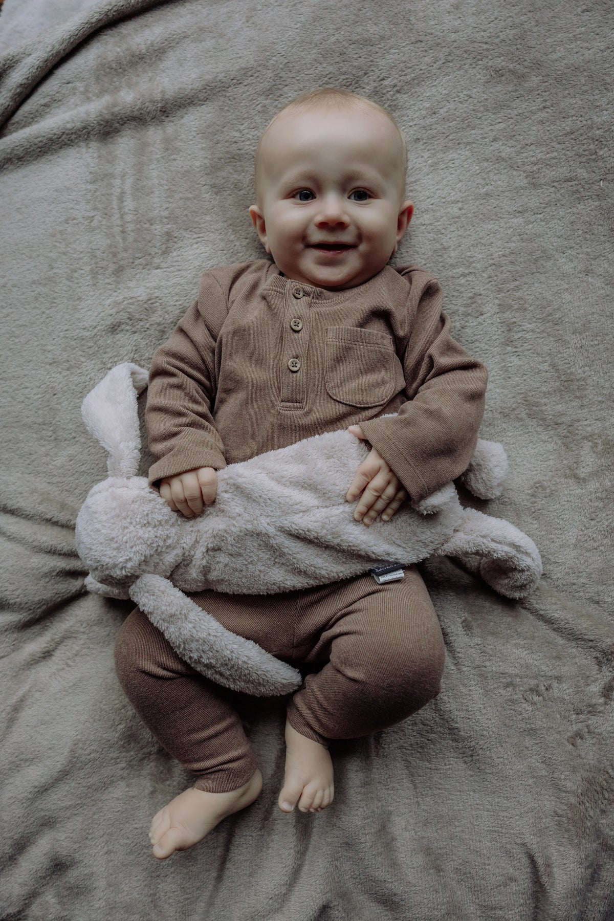 Smilende barn på et tæppe med Flow Amsterdam Milo varmebamse over maven.
