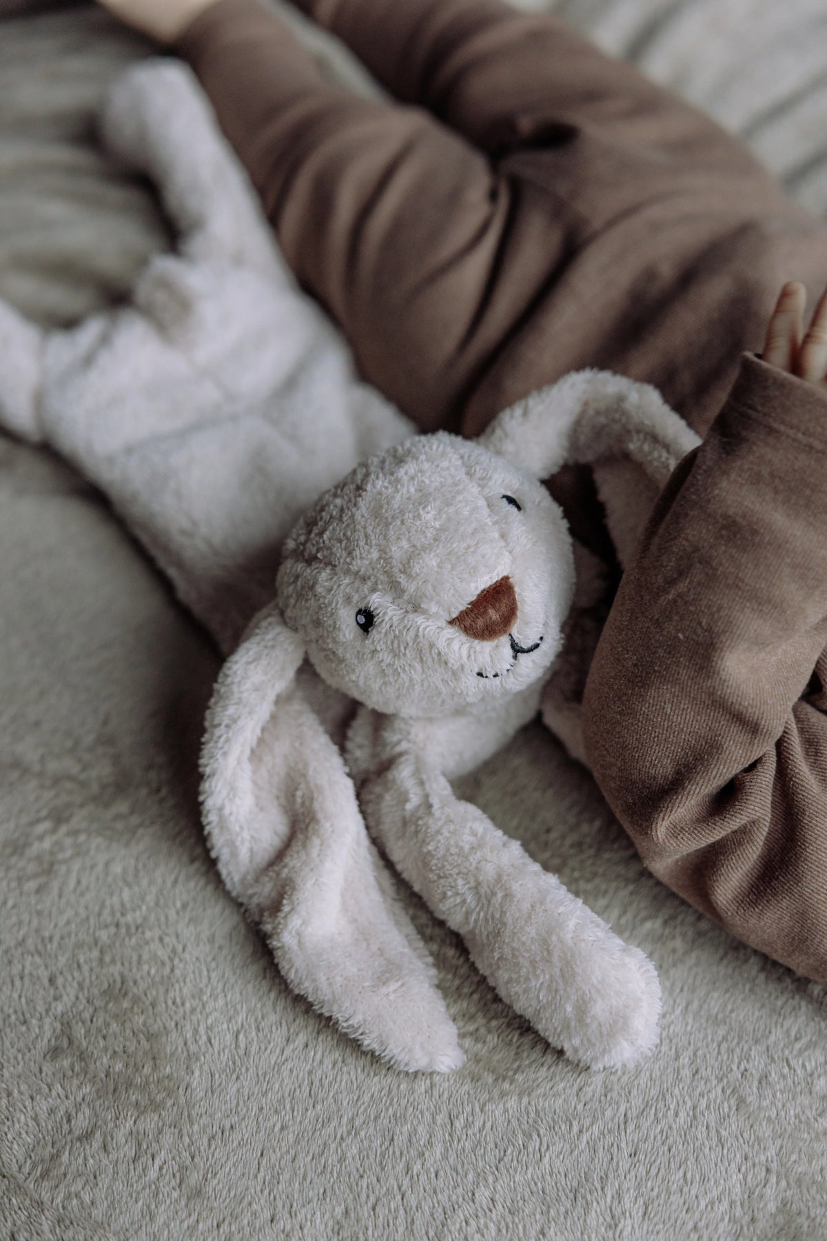 Nærbillede af Flow Amsterdam Milo kaninbamse ved siden af et barn på et tæppe.