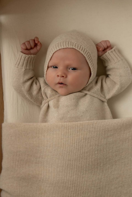 Nyfødt baby med merinould baby kyse fra Hvid i Cream ligger i sengen