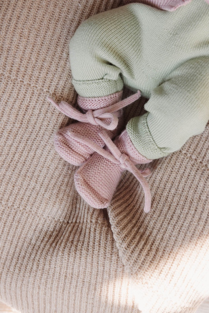 Baby med strikkede babyfutter fra Hvid i Powder på et strikket tæppe