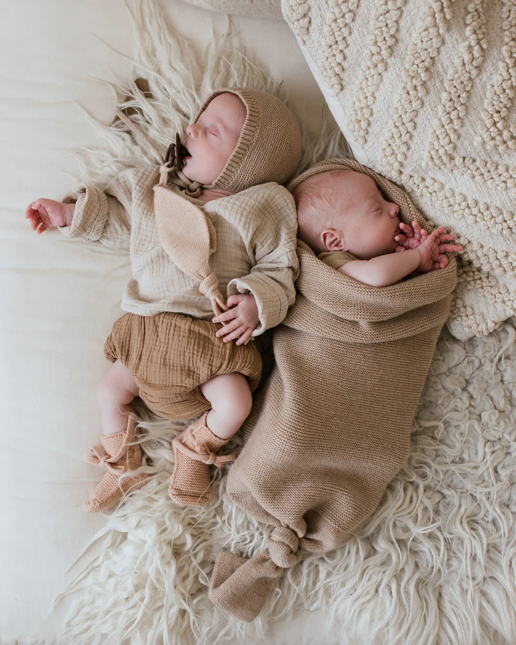 To babyer ligger ved siden af hinanden, den ene i Hvid merinould cocoon Sand med knude i bunden