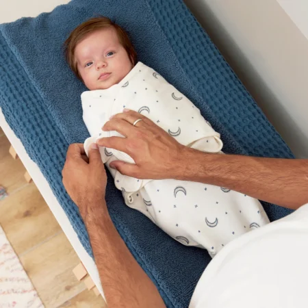 Nyfødt baby svøbt i blødt babysvøb med måne- og stjernemønster på puslepude.