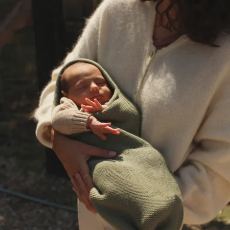 Baby svøbt i grønt baby svøb af merinould (Artichoke) fra Hvid, holdt trygt i mors arme.