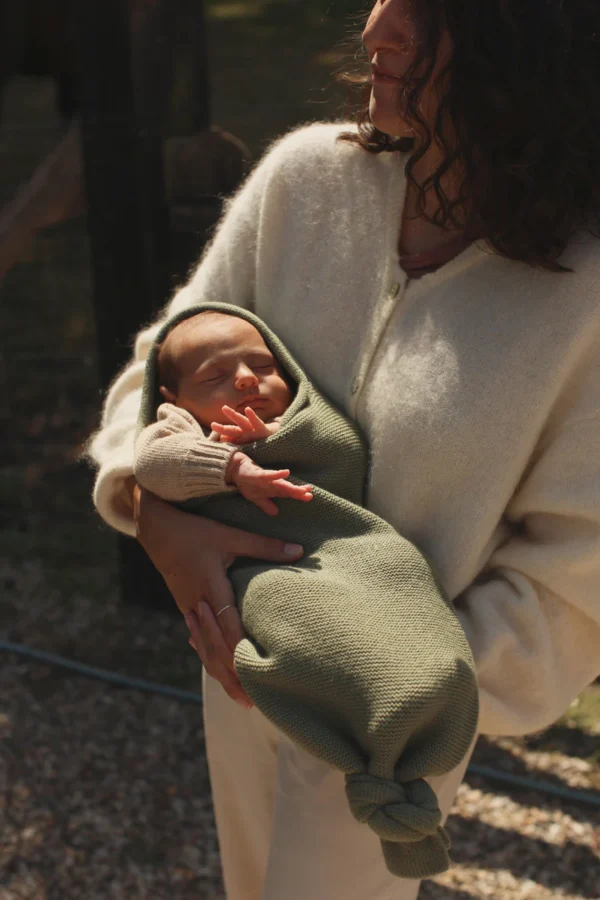 Baby svøbt i grønt baby svøb af merinould (Artichoke) fra Hvid, holdt trygt i mors arme.