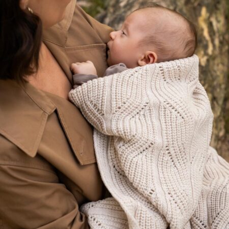 Mor holder baby svøbt i et beige merinould babytæppe – blødt, varmt og åndbart