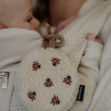Flow Amsterdam Comforter On The Go i mariehøne-design – blød hvid støj musikuro med hjertelyd, fastgjort til bæresele, Mrs. Mama.
