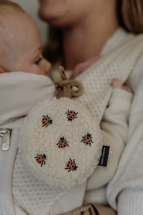 Flow Amsterdam Comforter On The Go i mariehøne-design – blød hvid støj musikuro med hjertelyd, fastgjort til bæresele, Mrs. Mama.