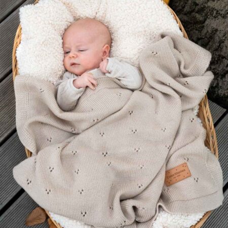 Baby ligger trygt i kurv med et blødt beige uld tæppe til baby i merinould – naturligt og åndbart tæppe til baby