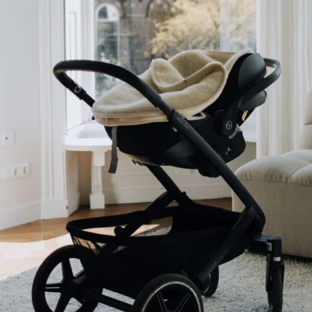 Kørepose i merinould placeret i autostol på stel indendørs, som viser den bløde og temperaturregulerende komfort til baby.