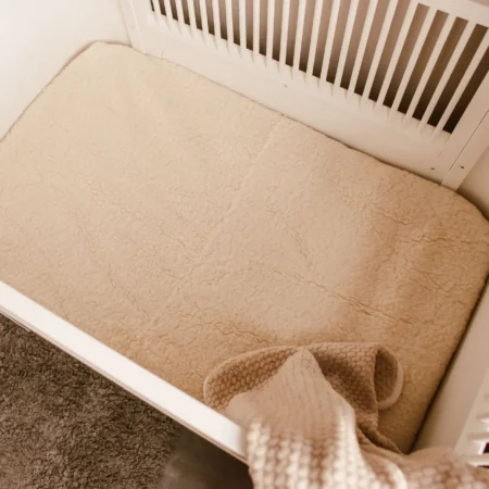 Lagen til tremmeseng i merinould, der skaber et naturligt og temperaturregulerende sovemiljø for baby