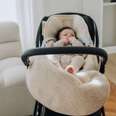Baby ligger trygt og varmt i en merinould kørepose til autostol i farven naturel, designet til autostol og Maxi-Cosi med 3-punktssele.